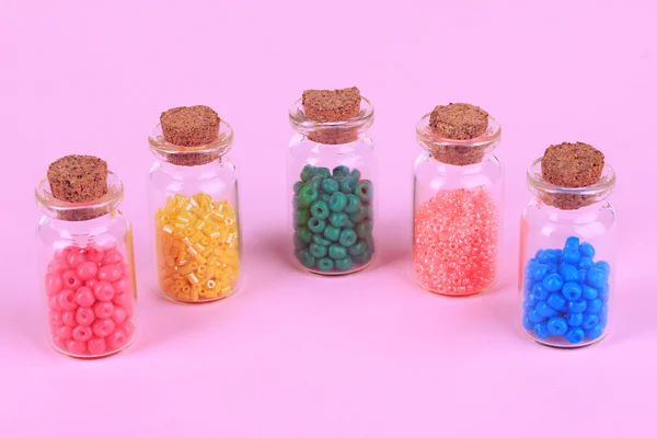 Verschiedene bunte Perlen in Flaschen auf beigem Hintergrund — Stockfoto