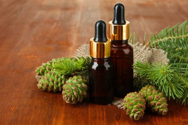 Bottles of fir tree oil and green cones on wooden background — Stock Photo, Image