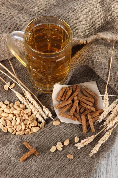 Bier in het glas, crackers en noten op zakken op houten tafel — Stockfoto