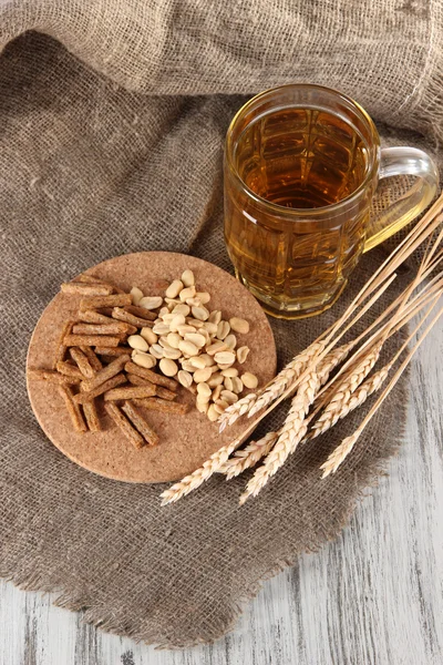 Bier in het glas, crackers en noten op zakken op houten tafel — Stockfoto