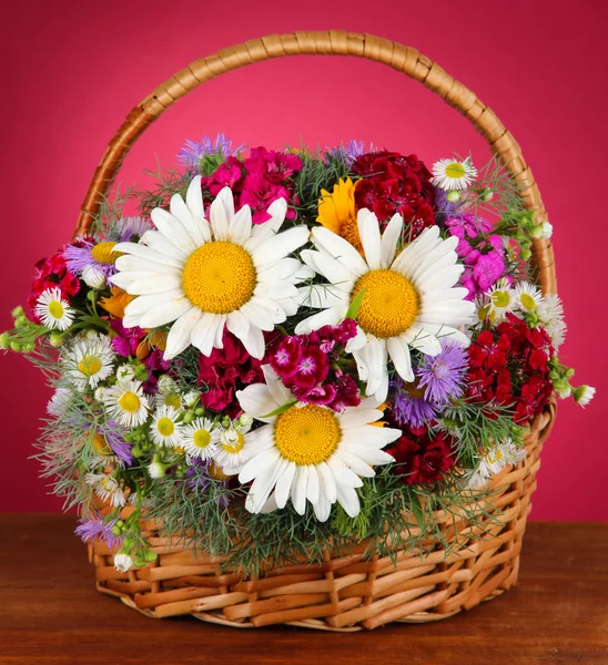 Beautiful bright flowers in wicker basket on table on pink background — Stock Photo, Image