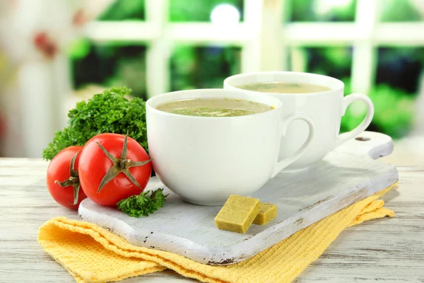 Cups of soup with bouillon cubes on wooden table — Stock Photo, Image