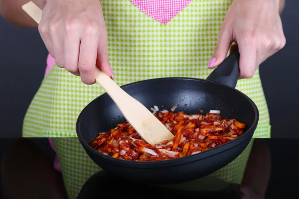 Hands cooking fried onion and carrot with tomatoes in pan on gray background — Stock Photo, Image