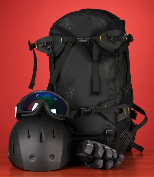 Winter sport glasses, helmet and gloves, backpack, on red background