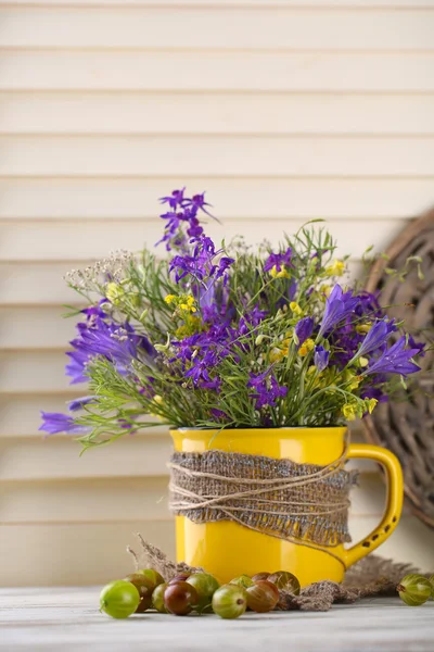 Mooi boeket van wilde bloemen in cup en bessen op houten tafel — Stockfoto