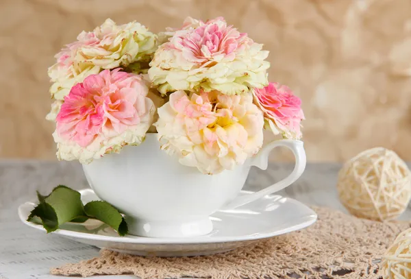 Roses in cup on napkins on wooden table on beige background — Stock Photo, Image
