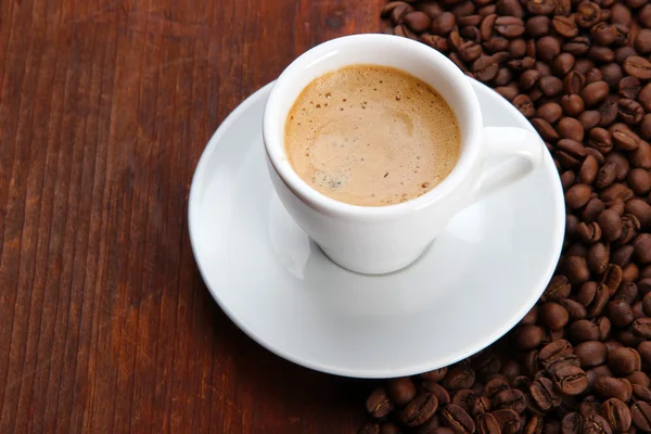 Чашка кави з кавовими зернами на дерев'яному фоні — стокове фото