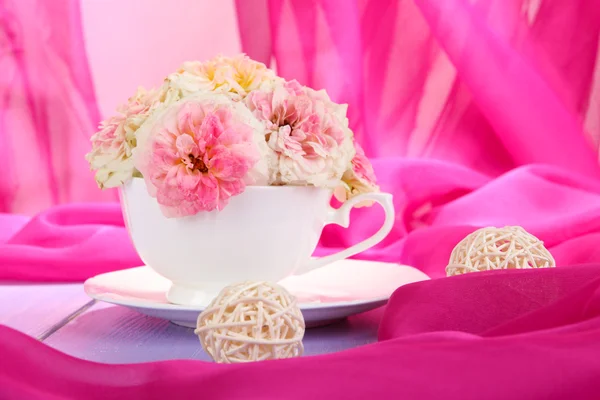 Rosen in Tasse auf Holztisch auf rosa Stoff Hintergrund — Stockfoto