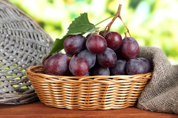Uvas maduras deliciosas en canasta de mimbre en la mesa sobre fondo brillante —  Fotos de Stock