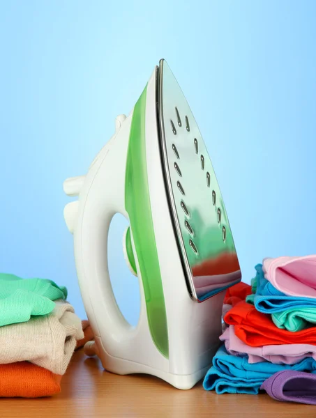 Steam iron with clothes, on color background — Stock Photo, Image