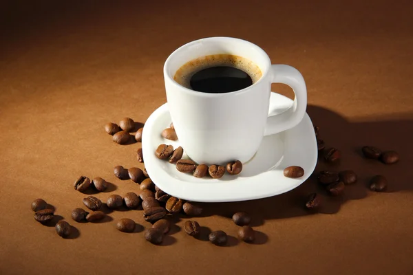 Secangkir kopi dengan biji kopi dengan latar belakang coklat — Stok Foto