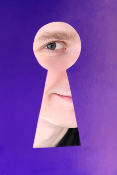 Человек глаз глядя через отверстие в замочной скважины, на голубом фоне — стоковое фото
