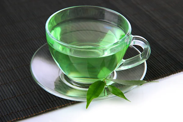 Taza transparente de té verde en estera de bambú, aislada en blanco — Foto de Stock