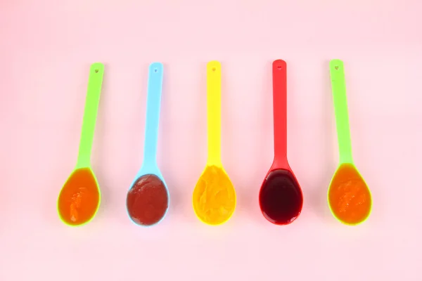 Baby puree in spoons on pink background — Stock Photo, Image