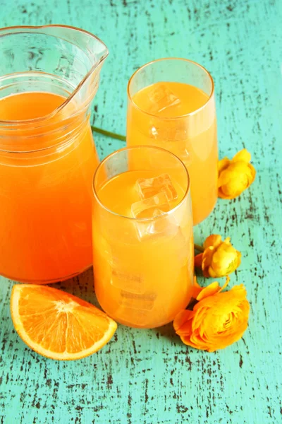 Vasos y jarra de zumo de naranja sobre fondo de madera azul — Foto de Stock