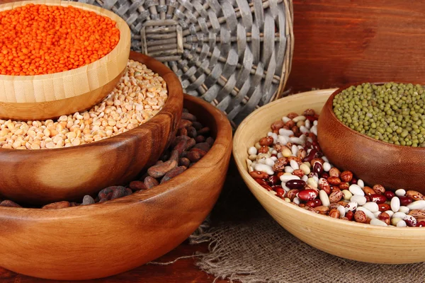 Different kinds of beans in bowls on wooden background — Stock Photo, Image