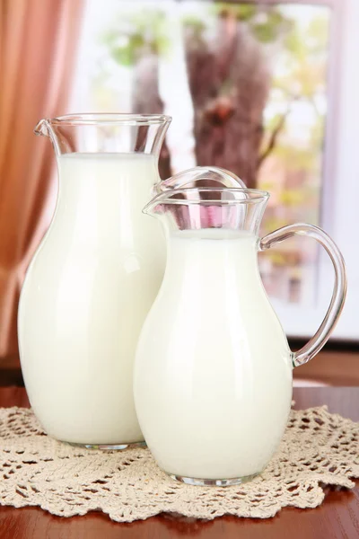 Pitchers of milk on table in room — Stock Photo, Image