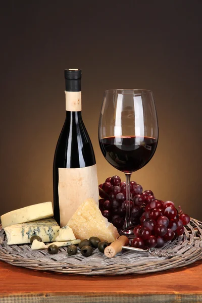 Viinin, juuston ja rypäleiden puhdistettu asetelma pajutarjottimella puupöydällä ruskealla pohjalla — kuvapankkivalokuva