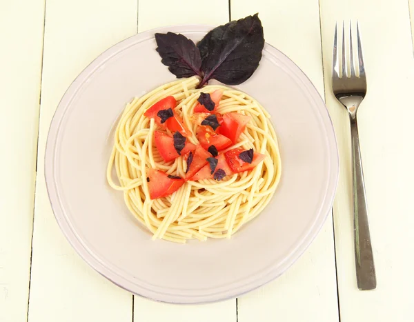 Spaghettis aux tomates et feuilles de basilic sur fond de bois — Photo