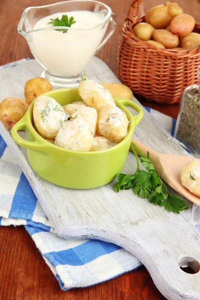 Tender young potatoes with sour cream and herbs in pan on wooden board on table close-up — Stock Photo, Image