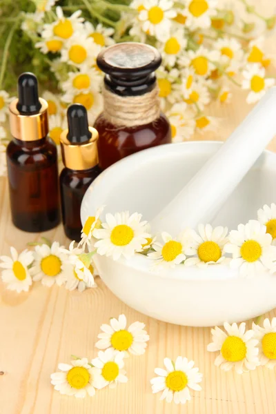 Aceite esencial y flores de manzanilla en mortero sobre mesa de madera —  Fotos de Stock