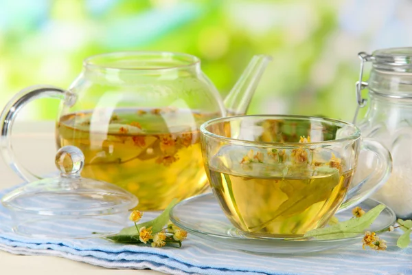 Wasserkocher und Tasse Tee mit Linde auf Serviette auf Holztisch auf Naturhintergrund — Stockfoto