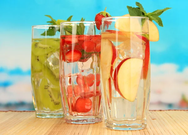 Glasses of fruit drinks with ice cubes on blue background — Stock Photo, Image