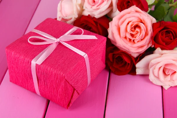 Beautiful bouquet of roses with gift on table close-up — Stock Photo, Image