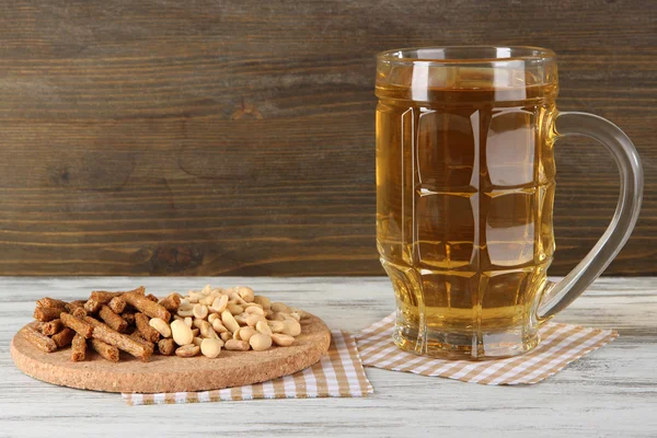 Beer in glass crunches, and nuts on napkin on table on wooden background — Stock Photo, Image