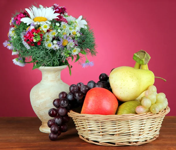 Vakre, lyse blomster i vase med frukt på bordet på rosa bakgrunn – stockfoto