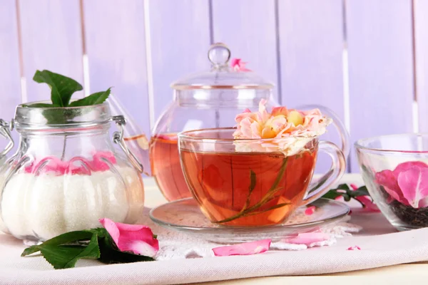 Чайник и чашка чая из чайной розы на салфетке на деревянном фоне — стоковое фото