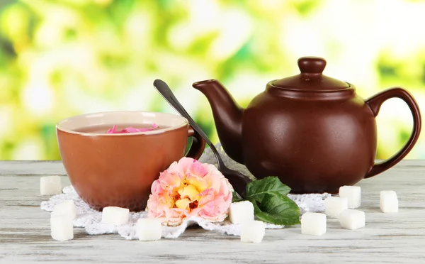 Wasserkocher und Tasse Tee aus Teerose an Bord auf Serviette auf Holztisch — Stockfoto