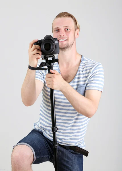 Bello fotografo con macchina fotografica su monopiede, su sfondo grigio — Foto Stock