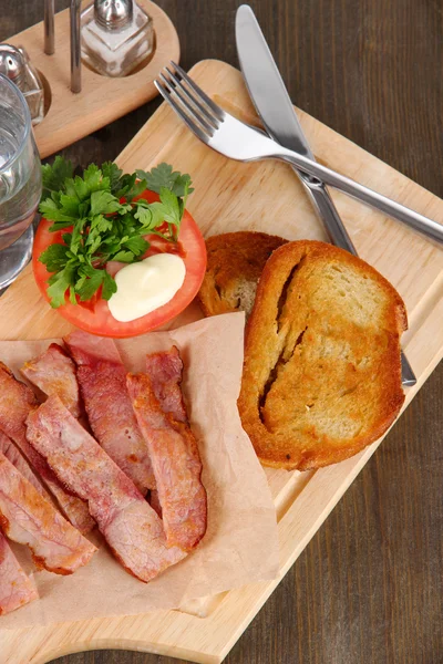 Bacon on plates on board on wooden table — Stock Photo, Image