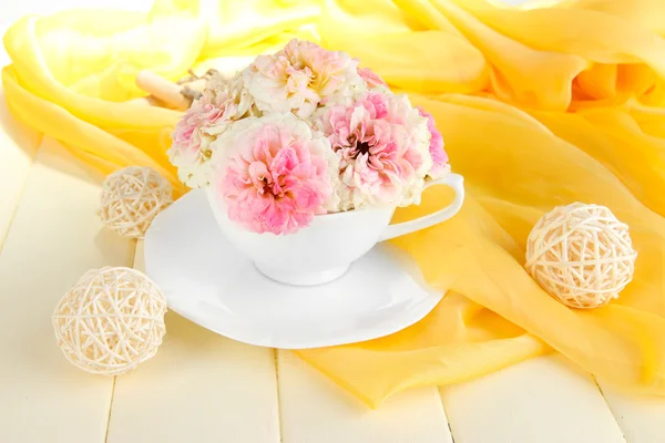 Rosas na xícara na mesa de madeira no fundo pano amarelo — Fotografia de Stock