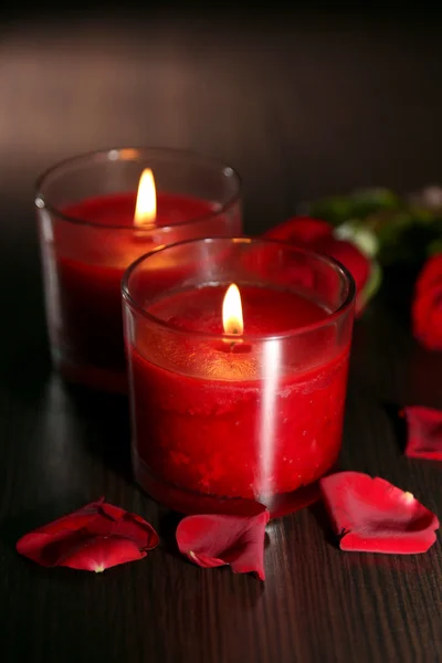 Belas velas vermelhas românticas com pétalas de flores no fundo de madeira escura — Fotografia de Stock