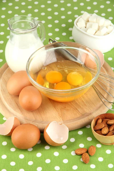 Broken egg in bowl and various ingredients next to them on green tablecloth close-up — Stock Photo, Image