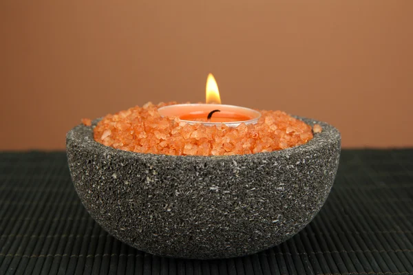 Candle in stone bowl with marine salt, on bamboo mat, on brown background — Stock Photo, Image