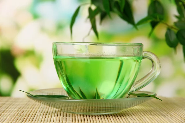 Tasse transparente de thé vert sur tapis de bambou, sur fond de nature — Photo