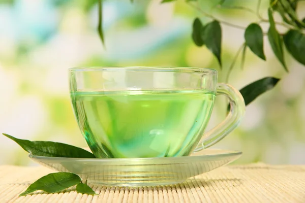 Xícara transparente de chá verde no tapete de bambu, no fundo da natureza — Fotografia de Stock