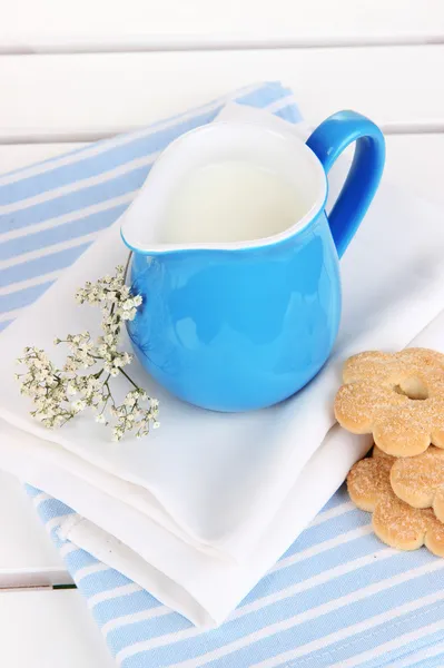 Blue jug with milk and cookies on wooden picnic table close-up — Stock Photo, Image