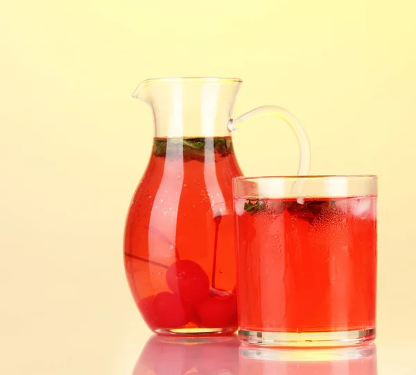 Kirschgetränk in Krug und Glas auf gelbem Hintergrund — Stockfoto