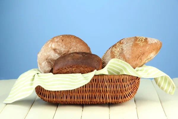 Bread in wicker basket, on wooden table, on color background — Stock Photo, Image