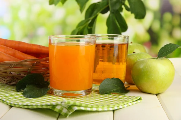 Glasses of juice, apples and carrots on white wooden table, on green background — Stock Photo, Image