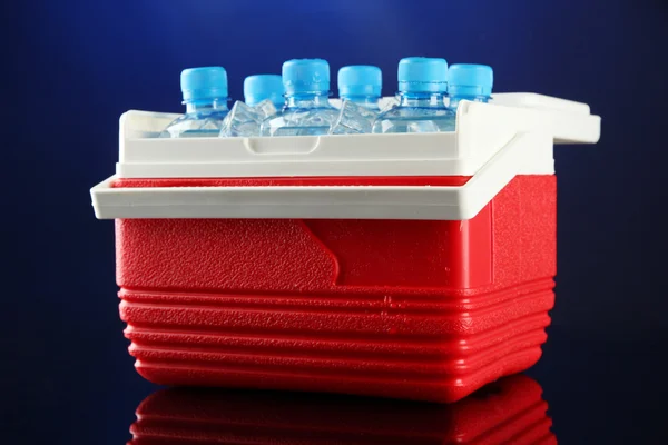 Reizende koelkast met flessen water en ijsblokjes, op blauwe achtergrond — Stockfoto
