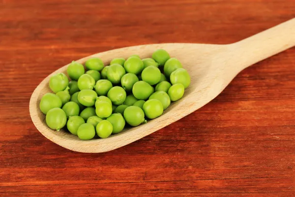 Guisantes verdes dulces en cuchara sobre fondo de madera — Foto de Stock