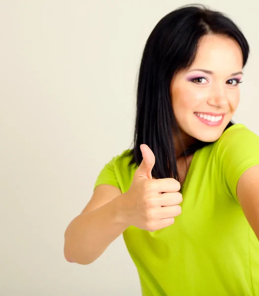 Mujer joven feliz mostrando el pulgar hacia arriba signo sobre fondo gris —  Fotos de Stock