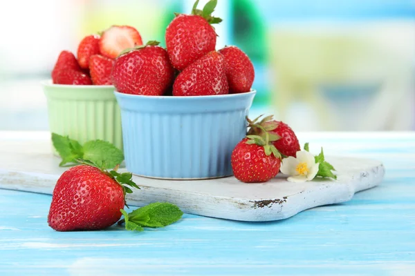 Rijpe zoete aardbeien in kommen op blauwe houten tafel — Stockfoto