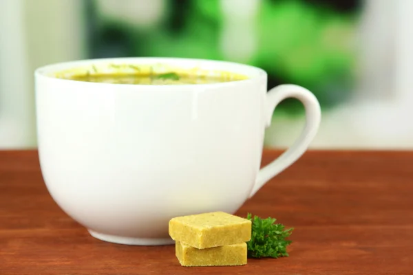 Copa de sopa con cubos de caldo sobre mesa de madera — Foto de Stock