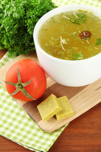 Kopje soep met bouillonblokjes op houten tafel — Stockfoto